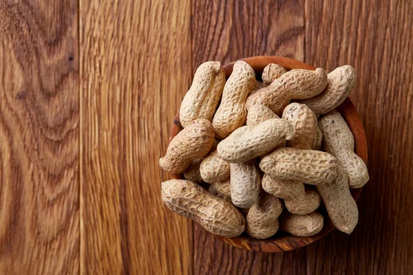 Unpeeled peanuts in wooden bowl over rustic wooden background closeup, selective focus