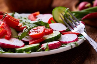 Yaratıcı taze sebze salatası ruccola, salatalık, domates ve beyaz plaka, seçici odak üzerinde raddish