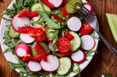 Yaratıcı taze sebze salatası ruccola, salatalık, domates ve beyaz plaka, seçici odak üzerinde raddish