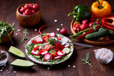 Yaratıcı taze sebze salatası ruccola, salatalık, domates ve beyaz plaka, seçici odak üzerinde raddish