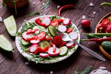 Yaratıcı taze sebze salatası ruccola, salatalık, domates ve beyaz plaka, seçici odak üzerinde raddish