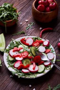 Yaratıcı taze sebze salatası ruccola, salatalık, domates ve beyaz plaka, seçici odak üzerinde raddish