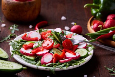 Yaratıcı taze sebze salatası ruccola, salatalık, domates ve beyaz plaka, seçici odak üzerinde raddish