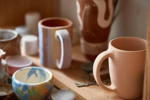 Tazas de alfarero hechas a mano y tazón de pintura en un estante de madera, primer plano, profundidad compañero de campo . — Foto de Stock