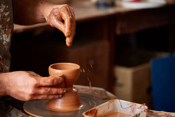 Close-up van de handen van een mannelijke potter in schort het morsen van wat water terwijl het maken van een vaas van klei, selectieve aandacht — Stockfoto