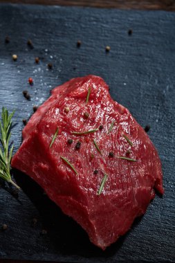 Çiğ et dana biftek siyah üzerine kurulu baharat ve biberiye ile ahşap arka plan üzerinde seçici odak kayrak