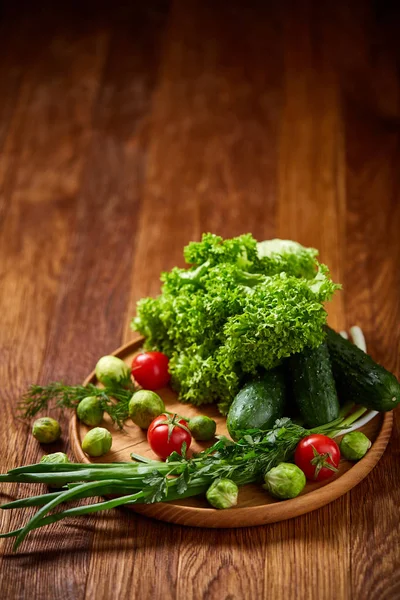 Nature morte végétarienne de légumes frais sur assiette en bois sur fond rustique, gros plan, plat . — Photo