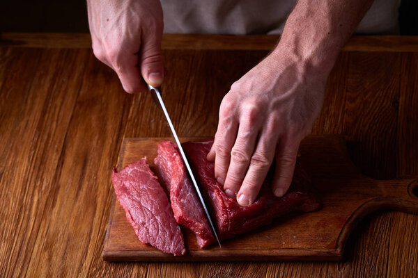 Strong professional mans hands cutting raw beefsteak, selective focus, close-up