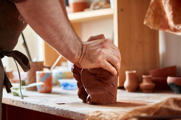 Adult male potter master modeling the clay plate on potters wheel. Top view, closeup, hands only.