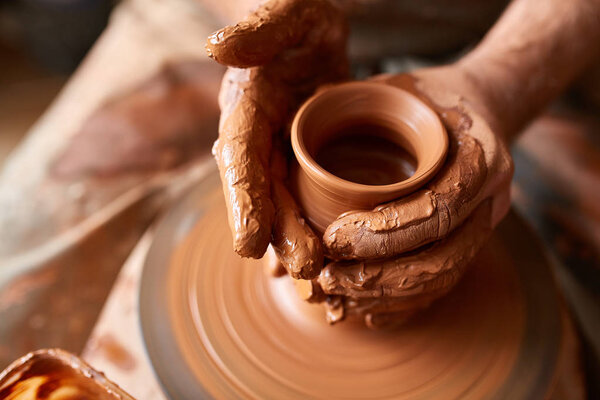 Close-up hands of a male potter in apron making a vase from clay, selective focus