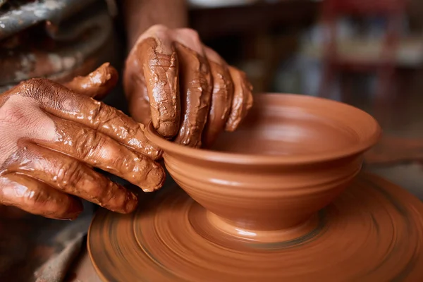 Close-up hands of a male potter in apron making a vase from clay, selective focus