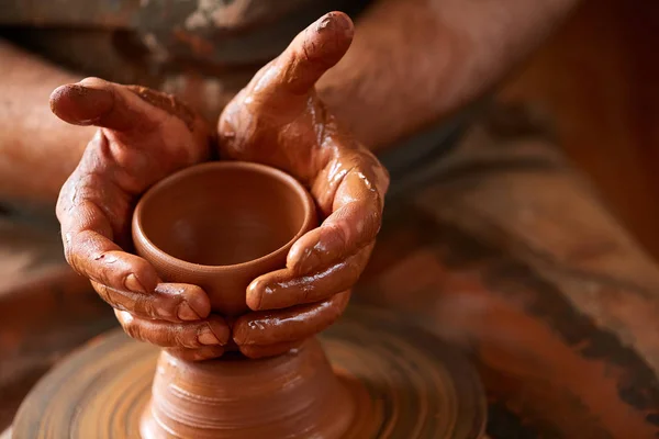 Primo piano mani di un vasaio maschio in grembiule rendendo un vaso di argilla, messa a fuoco selettiva — Foto Stock