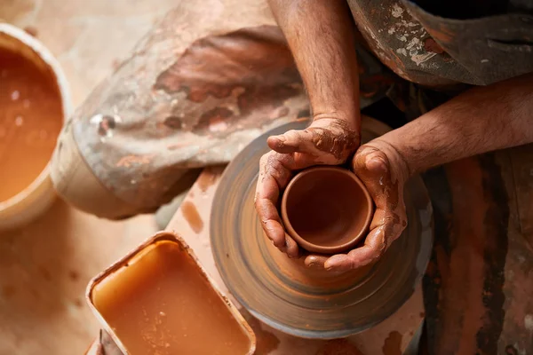 Close-up mãos de um oleiro masculino em avental fazendo um vaso de barro, foco seletivo — Fotografia de Stock