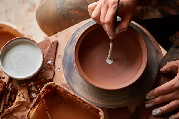 Een pottenbakker schildert een kleiplaat in een wit in de workshop, bovenaanzicht, close-up, selectieve focus. — Stockfoto