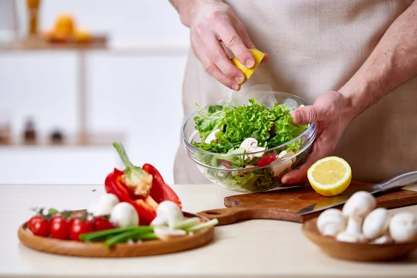 Man cooking at kitchen making healthy vegetable salad, close-up, selective focus.