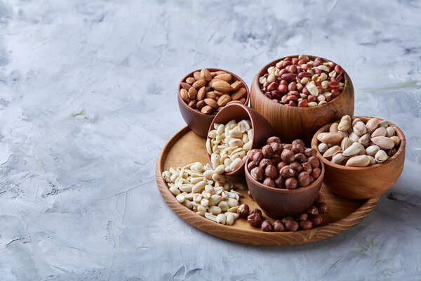 Mixed nuts in brown bowls on wooden tray over white background, close-up, top view, selective focus.