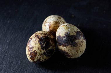 Üç Bıldırcın yumurta bir koyu arka plan, üstten görünüm, yakın çekim, seçici odak grup, uzay kopyalayın, aydınlatma.