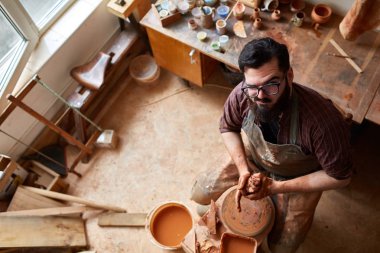 Portrait of a male potter in apron molds bowl from clay, selective focus, close-up clipart
