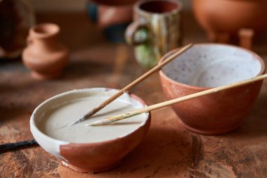Boya fırçaları ahşap bir çömlekçi atölye, yakın çekim, seçici odak üzerinde seramik kase daldırma.