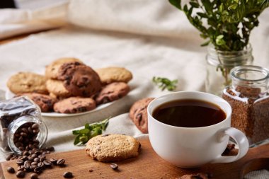 Kahve fincanı, kavanoz kahve çekirdekleri, Çerezler üzerinde saf masa örtüsü, seçici odak, yakın çekim, en iyi görünümü ile