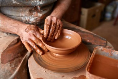 Close-up hands of a male potter in apron molds bowl from clay, selective focus clipart