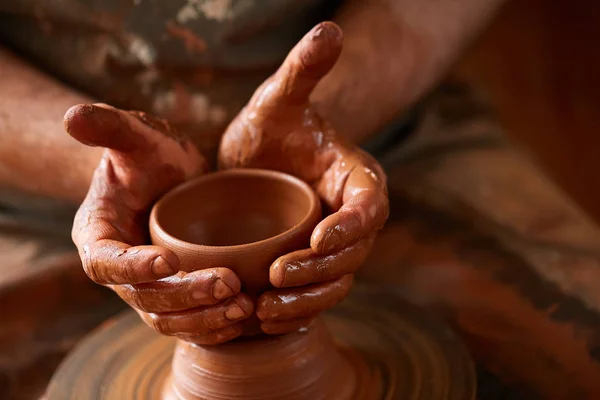 Close-up hands of a male potter in apron molds bowl from clay, selective focus