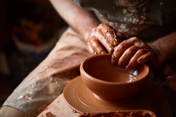 Close-up hands of a male potter in apron molds bowl from clay, selective focus