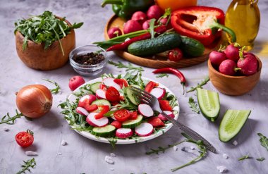 Yaratıcı taze sebze salatası ruccola, salatalık, domates ve beyaz plaka, seçici odak üzerinde raddish