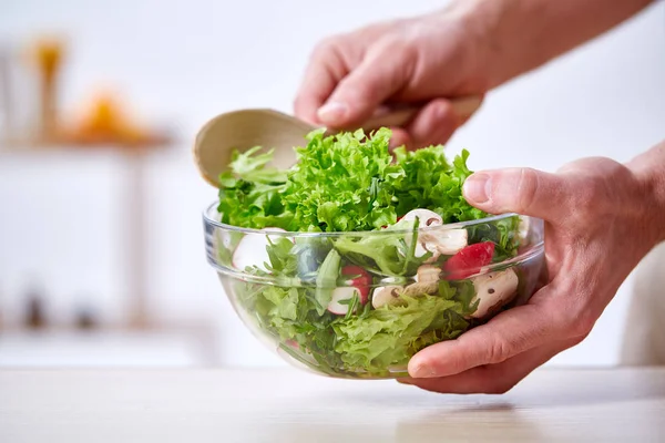 Uomo che cucina in cucina facendo insalata di verdure sana, primo piano, messa a fuoco selettiva . Foto Stock Royalty Free