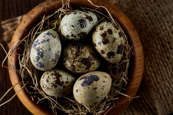 Huevos frescos de codorniz en un tazón de madera en una servilleta hecha en casa sobre fondo de madera oscura, vista superior, primer plano — Foto de Stock