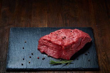 Çiğ et dana biftek siyah üzerine kurulu baharat ve biberiye ile ahşap arka plan üzerinde kopya alanı kayrak