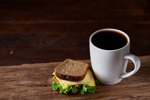 Table de petit déjeuner avec sandwich et café noir sur fond bois rustique, gros plan, mise au point sélective — Photo