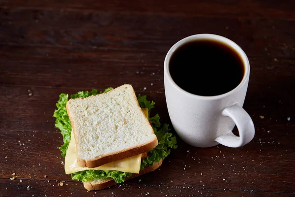 Breakfast table with sandwich and black coffee on rustic wooden background, close-up, selective focus — Stock Photo, Image