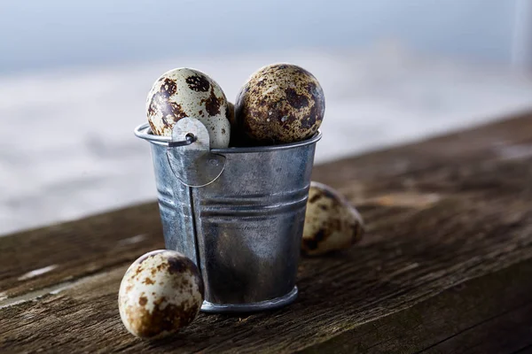 Small decorative bucket filled with quail eggs on napkin over white textured background, close-up, selective focus. — Stock Photo, Image