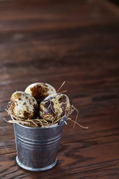 Small decorative bucket filled with quail eggs dark wooden table, close-up, selective focus. — Stock Photo, Image