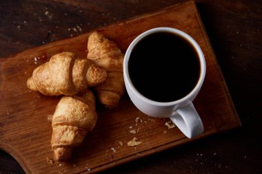 Kruvasan ve ahşap kesme tahtası üzerinde siyah kahve ile kahvaltı rustik arka plan, yakın çekim, seçici odak üzerinde