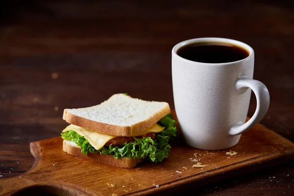 Сніданок з бутербродом і чорною кавою на дерев'яній обробній дошці на сільському фоні, крупним планом, вибірковий фокус — стокове фото