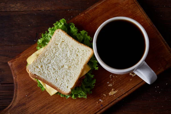 Mesa de desayuno con sándwich y café negro sobre tabla de cortar de madera sobre fondo rústico, primer plano, enfoque selectivo — Foto de Stock