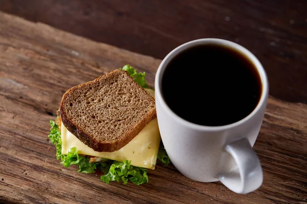 Mesa de desayuno con sándwich y café negro sobre fondo rústico de madera, primer plano, enfoque selectivo — Foto de Stock
