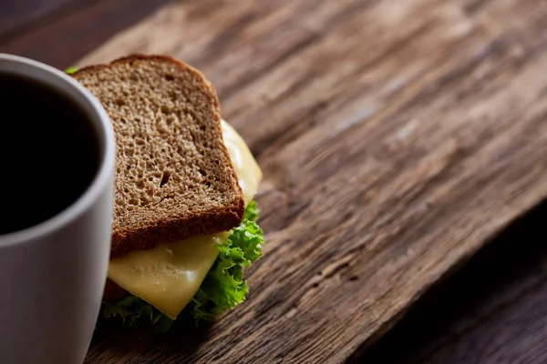 Table de petit déjeuner avec sandwich et café noir sur fond bois rustique, gros plan, mise au point sélective — Photo