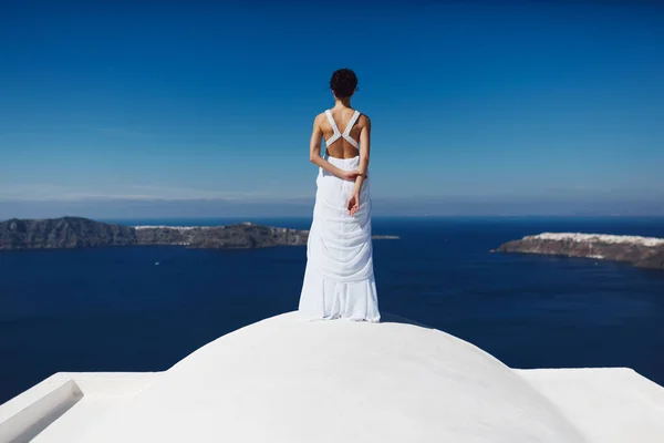 The bride stands turned away on the white roof of the house. Beautiful views of the blue sea, sky and islands.