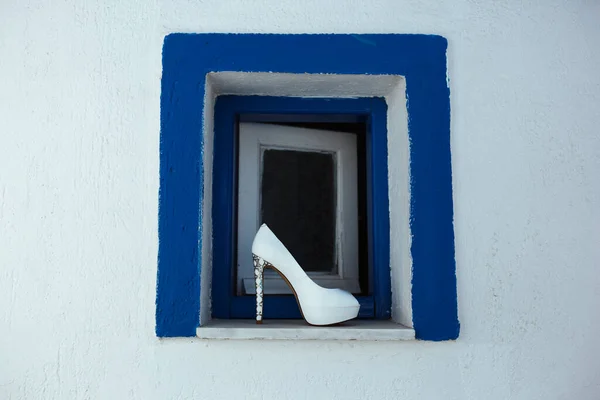 Bir kadın beyaz ayakkabı mavi kenarlı küçük bir pencerede duruyor.