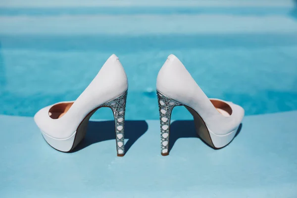 Havuzun kenarında beyaz topuklu ayakkabılar var.