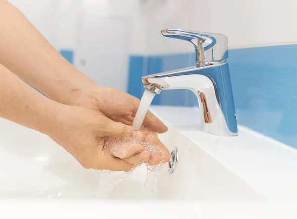 Kız ellerini banyoda akan suyun altında yıkıyor.