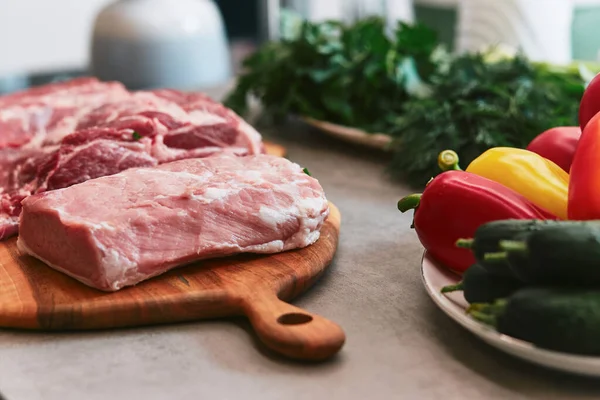 Kesme tahtasının üzerinde birkaç parça et var. Tahtanın yanında salatalık, domates, biber, maydanoz, soğan, dereotu ve kişniş tabakları var. Yüksek kalite fotoğraf