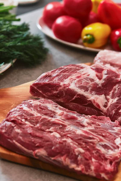 Kesme tahtasının üzerinde birkaç parça et var. Tahtanın yanında salatalık, domates, biber, maydanoz, soğan, dereotu ve kişniş tabakları var. Yüksek kalite fotoğraf