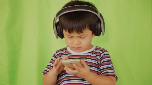 Χαριτωμένο μικρό αγόρι που στέκεται στο στούντιο ενώ ακούτε μουσική στο smartphone με το ακουστικό. — Αρχείο Βίντεο