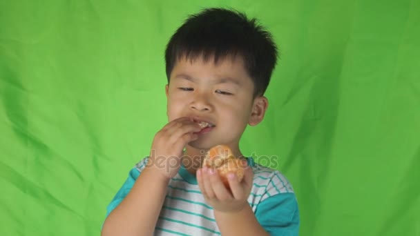 Leuke jongen eten oranje op groene achtergrond, — Stockvideo