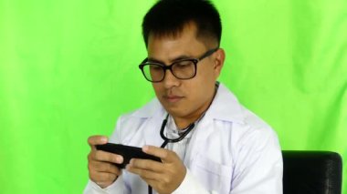 Asyalı erkek doktor smartphone cep telefonu ile Office yeşil zemin üzerine oyun oynama,