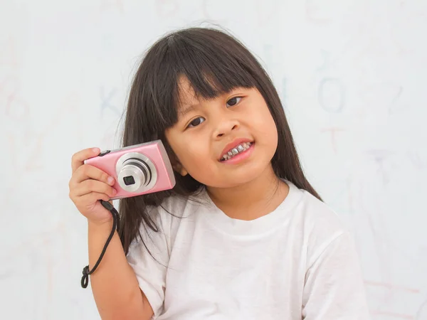 Smiling young girl holding photo camera on wall background — Stock Photo, Image